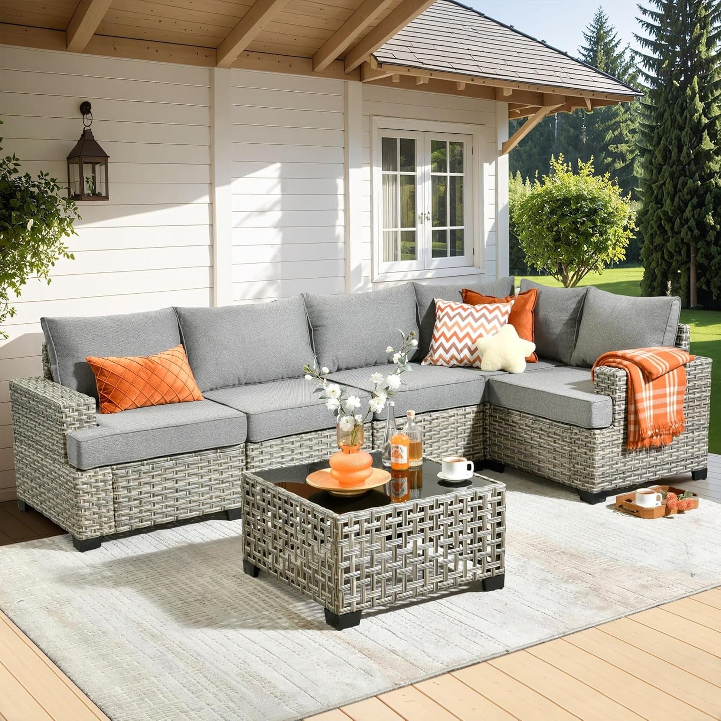 Outdoor patio set with gray sofa, orange cushions, and a small table on a wooden deck.