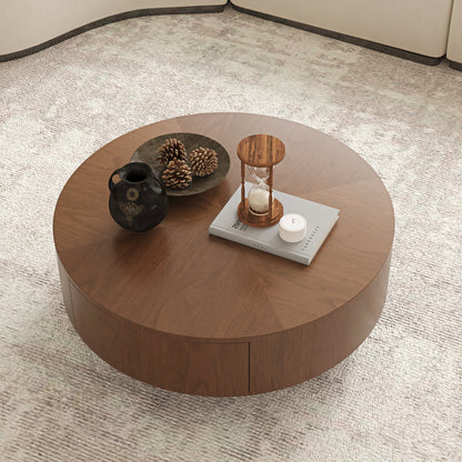 A round wooden coffee table with a warm medium-brown finish, styled with a black ceramic vase, pinecones, a small hourglass, and a candle on a light beige textured rug.