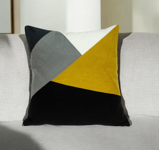 Geometrically patterned pillow with black, yellow, and gray triangles on a sofa.