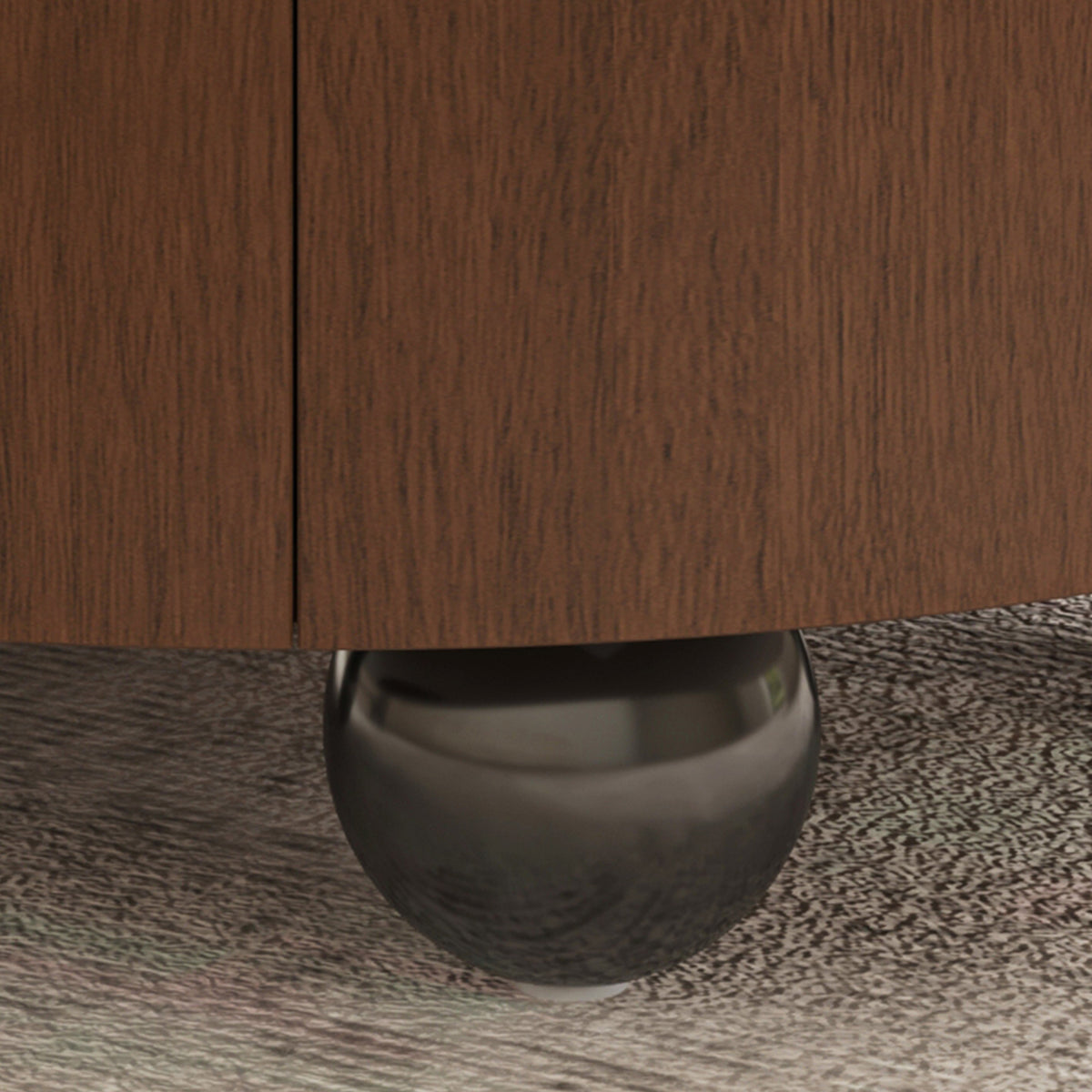 Close-up detail of a dark brown wood cabinet or dresser with a polished metallic ball support leg on a textured gray carpet.
