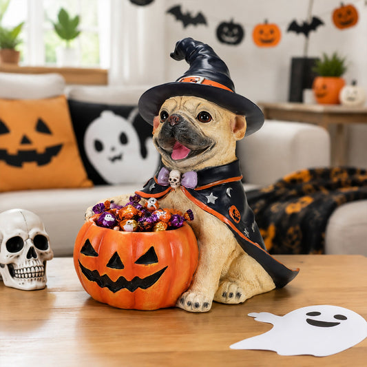 A decorative figurine of a pug dressed as a witch sitting in a pumpkin-shaped bowl filled with wrapped candy, placed on a wooden table in a Halloween-themed living room.