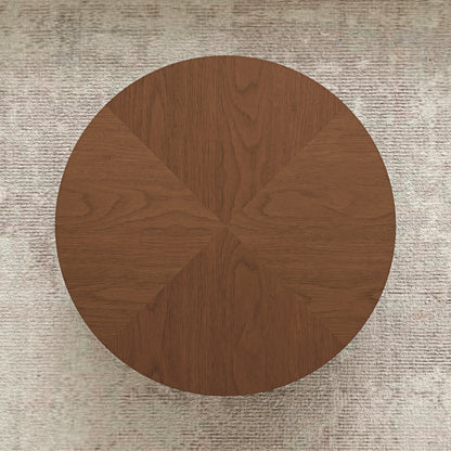 A round wooden coffee table viewed from directly above, featuring a warm medium-brown wood grain finish and a geometric segmented design radiating from the center, set against a textured light beige rug.