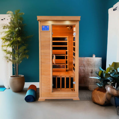 Wooden infrared sauna in a room with plants and a blue wall.