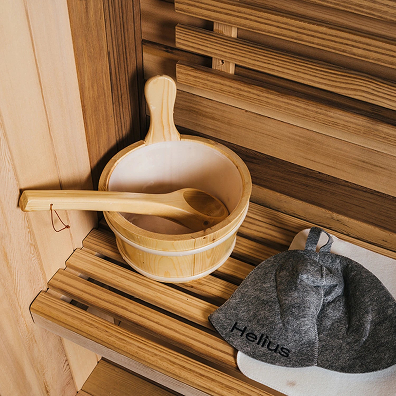 Wooden bucket and ladle on a wooden bench in a sauna with a gray towel labeled 'Helius'. 4–6 Person Cedar Barrel Sauna Room with Porch – Outdoor Home Garden Sauna. 076823-f9.myshopify.com